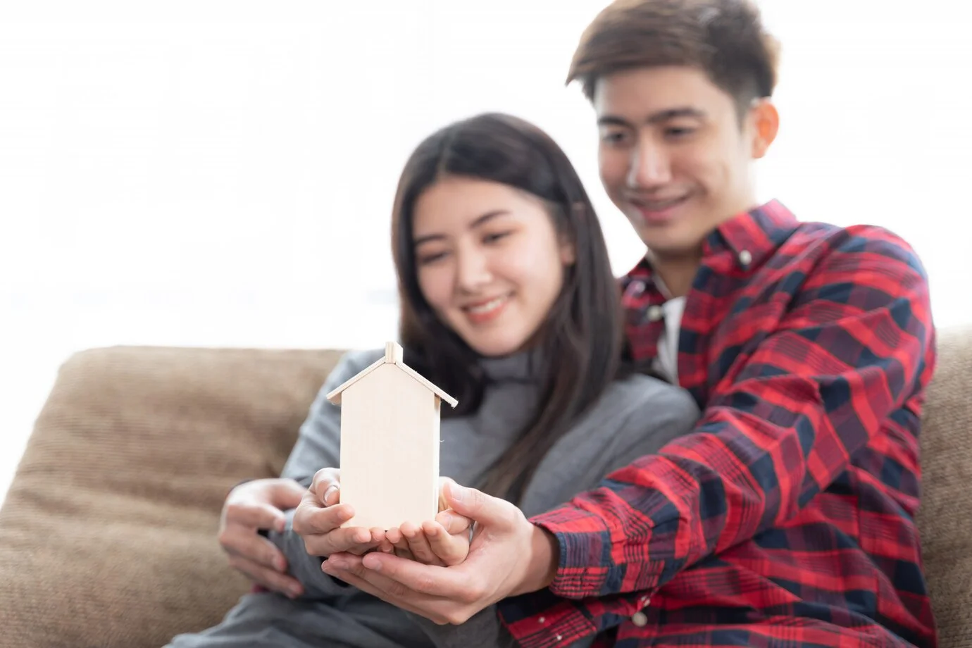 Couple holding a small wooden house model, planning for closing costs
